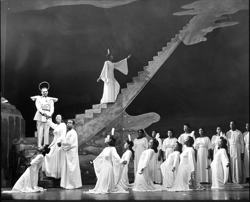 Black and White photo of the cast in the original 1943 Broadway production. The ensemble is dressed in all white robes while another cast member wears a halo and angel wings.